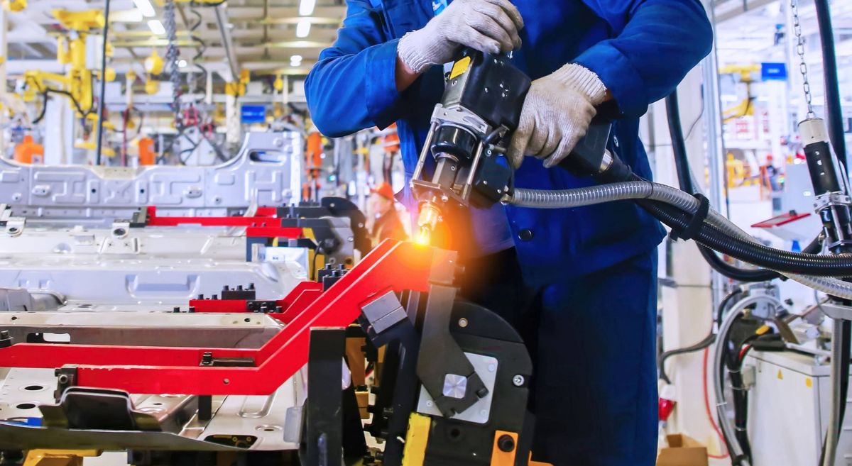 Worker operates robotic equipment for car manufacturing in an industrial facility during daytime