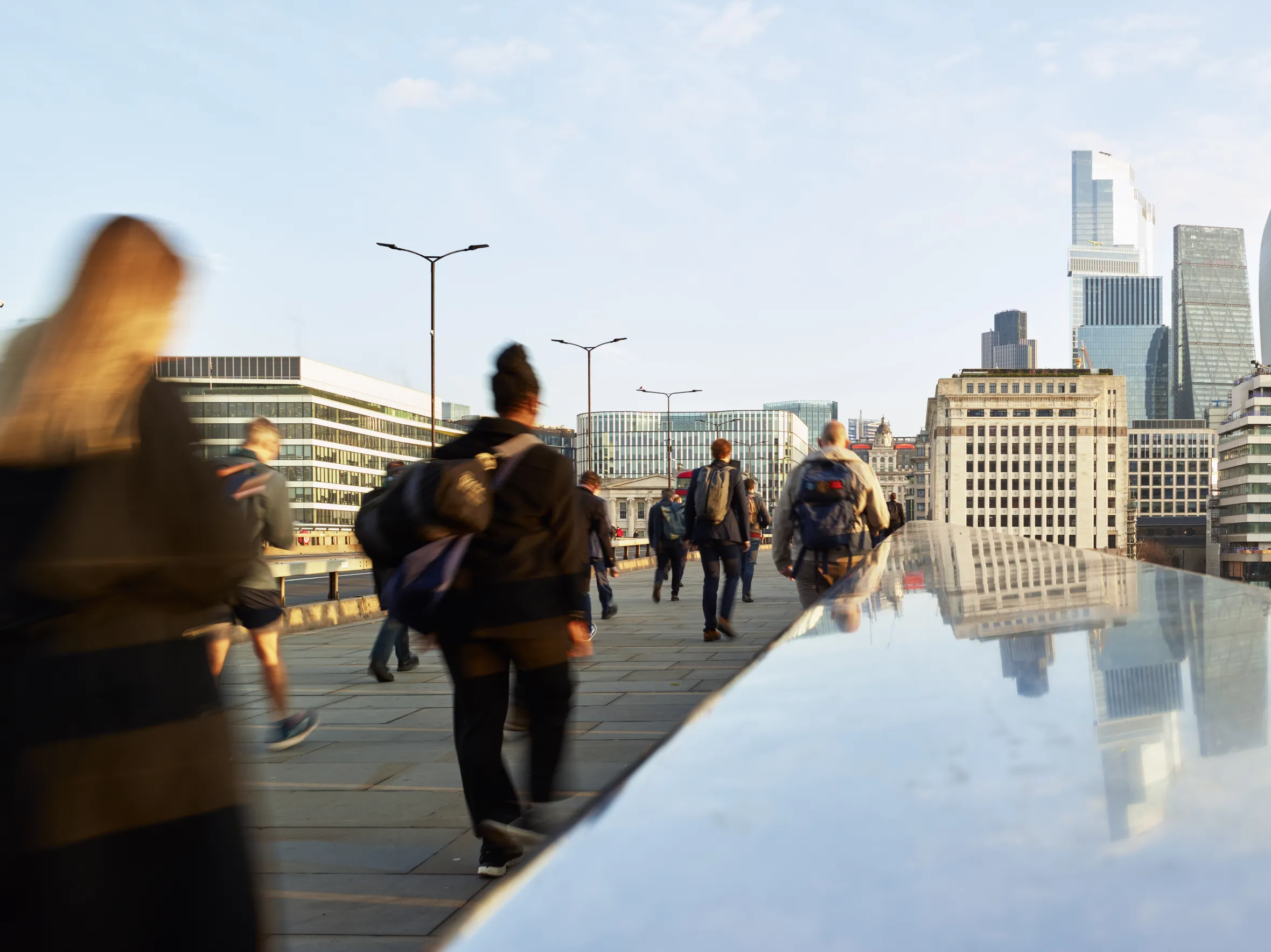 Blurred motion of business people walking to work on London Bridge with modern and traditional office buildings in the background.