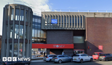 Front elevation of the building showing the circular stairs and branding of Virgin Money visible with couple of cars parked at the front.