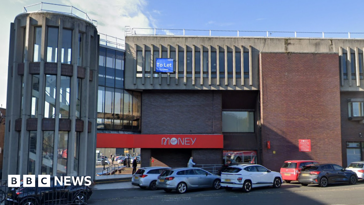Front elevation of the building showing the circular stairs and branding of Virgin Money visible with couple of cars parked at the front.