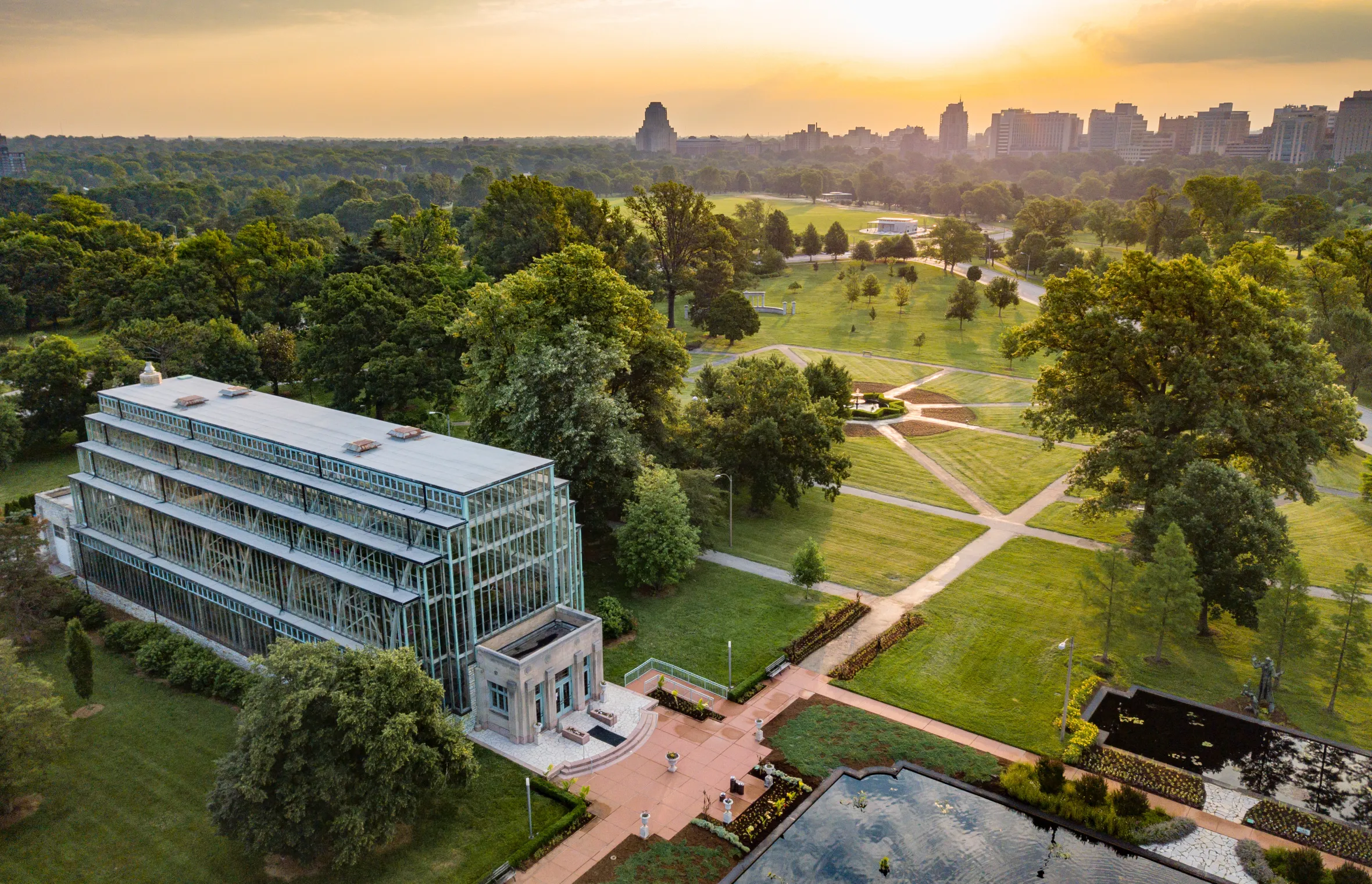 Aerial view of a greenhouse with a large park and city skyline in the background at sunset.