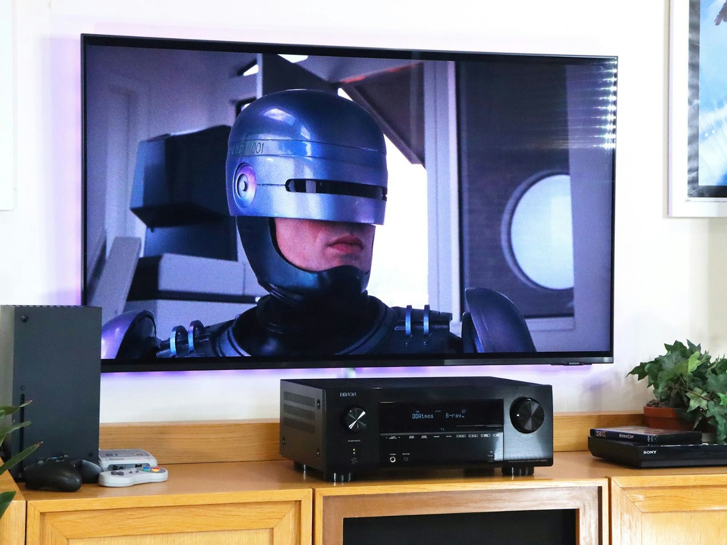 Denon AVR-X2800H Home Cinema Amplifier on a stand with Xbox and blu-ray player in front of a TV showing robocop