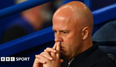 Headshot of Arne Slot, sitting on the bench, fingers on top lip, looking pensive