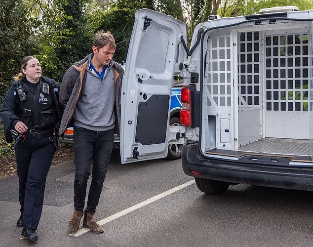 Resident James Evans is led away by police for 'obstructing an officer' after telling two locals to ignore their requests to move their cars which were preventing the lorry entering the field
