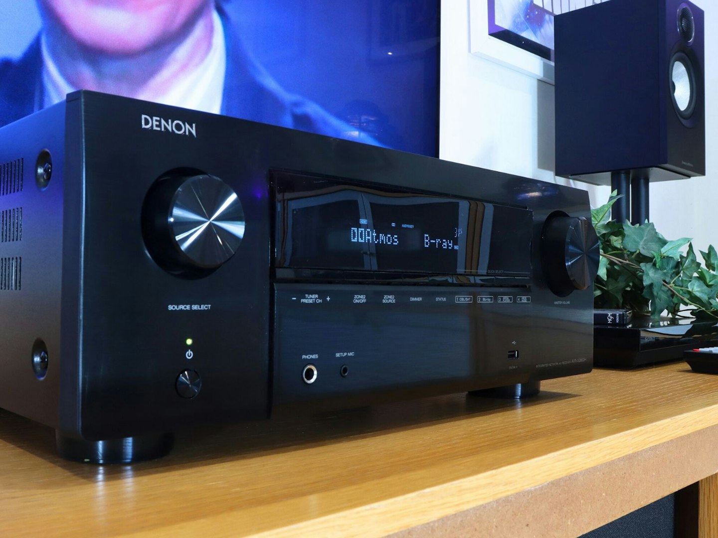 Denon AVR-X2800H Home Cinema Amplifier on a stand in front of a TV with a speaker in a living room