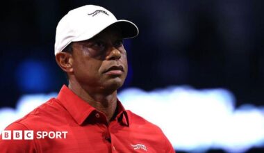 Tiger Woods wears a red T-shirt and a white cap
