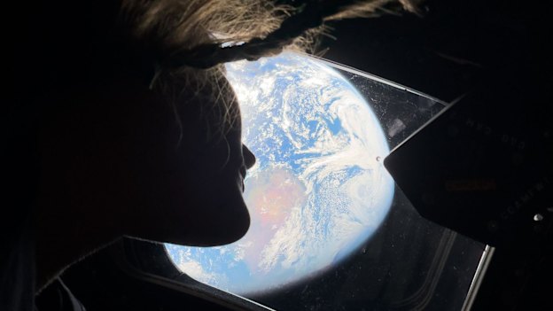 Christina Koch peers out of one of the Orion spacecraft’s main cabin windows, looking back at Earth.