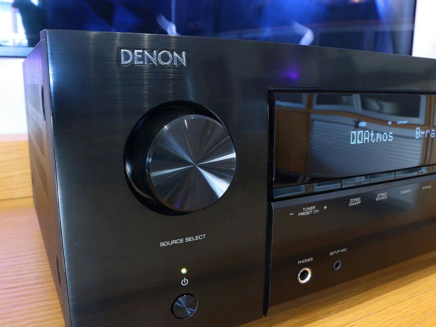 Denon AVR-X2800H Home Cinema Amplifier on a stand in front of a TV - front source control and display