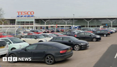 Cars parked in a Tesco car park. The entrance to the store is in the background.