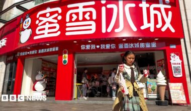 A shop of Mixue, a Chinese bubble tea brand in Chongqing, China in April 2026. In the foreground a girl walks away from the shop holding two sundaes and a drink.