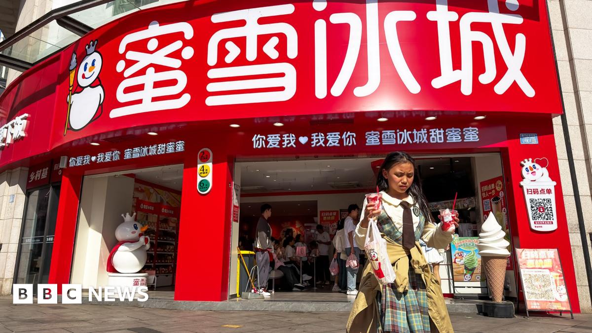 A shop of Mixue, a Chinese bubble tea brand in Chongqing, China in April 2026. In the foreground a girl walks away from the shop holding two sundaes and a drink.
