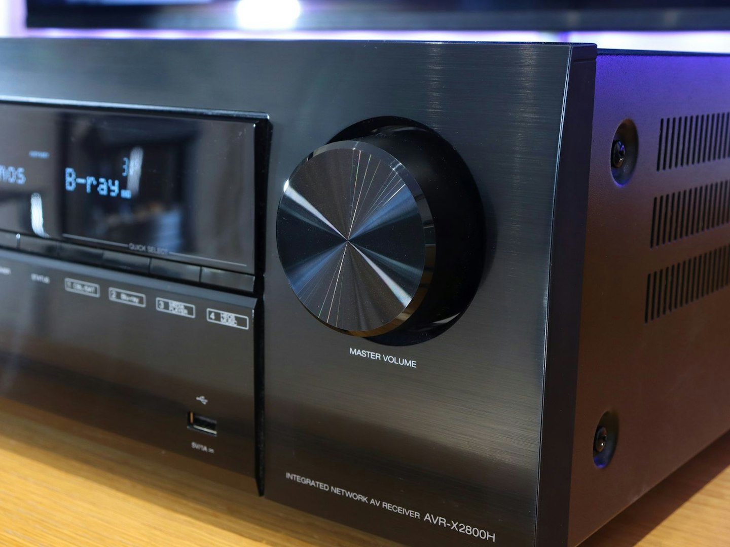 Denon AVR-X2800H Home Cinema Amplifier on a stand in front of a TV - front master volume control