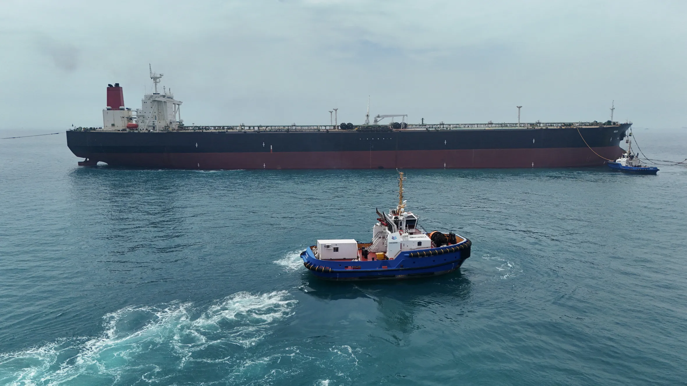 Drone view of the oil tanker HELGA berthed at an offshore terminal near Basra, Iraq, accompanied by a smaller blue and white tugboat.
