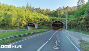 A stretch of road leading into a tunnel. It is a sunny day.
