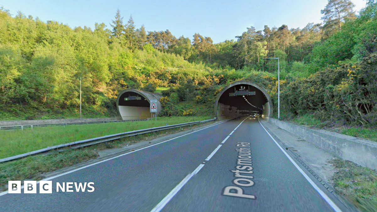 A stretch of road leading into a tunnel. It is a sunny day.