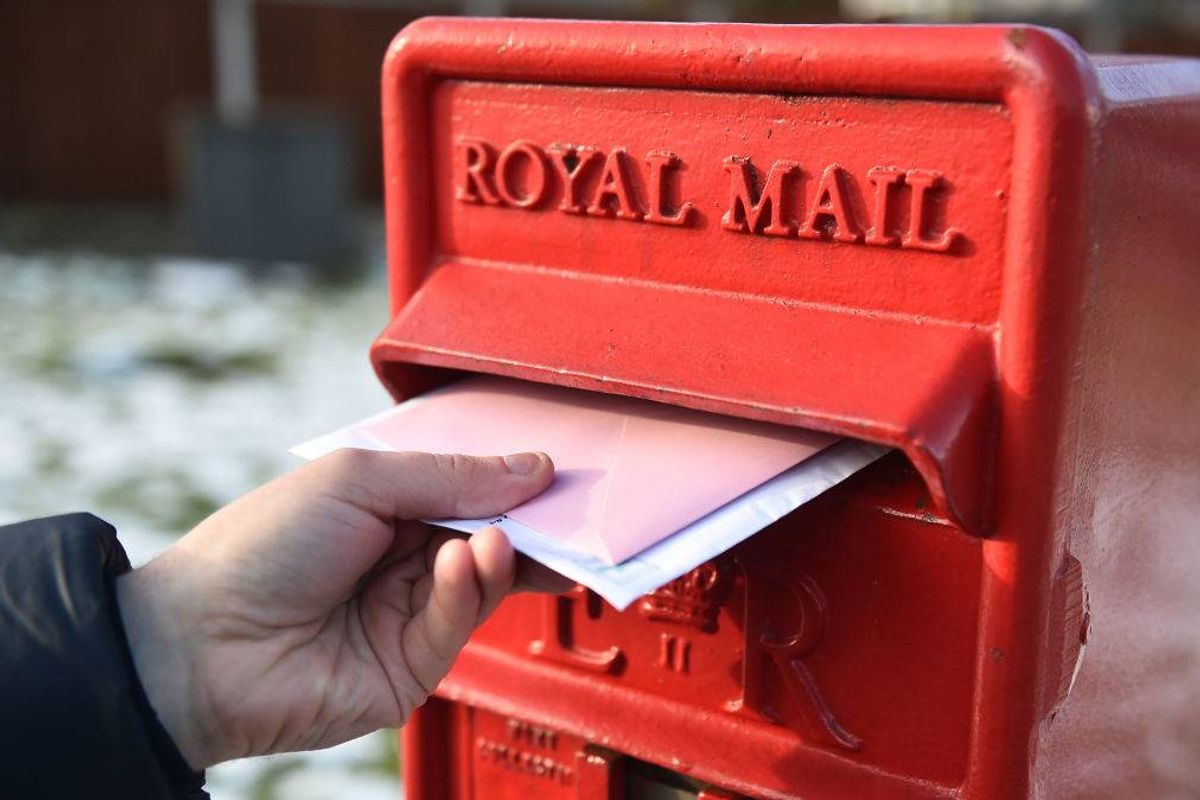 An individual is inserting a pink envelope into a red Royal Mail postbox against a snowy background.