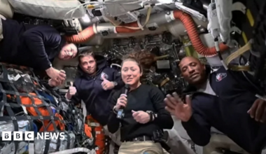 A section of the Orion spacecraft on the bottom left corner with the moon in the background filling the right side with half of it in darkness.