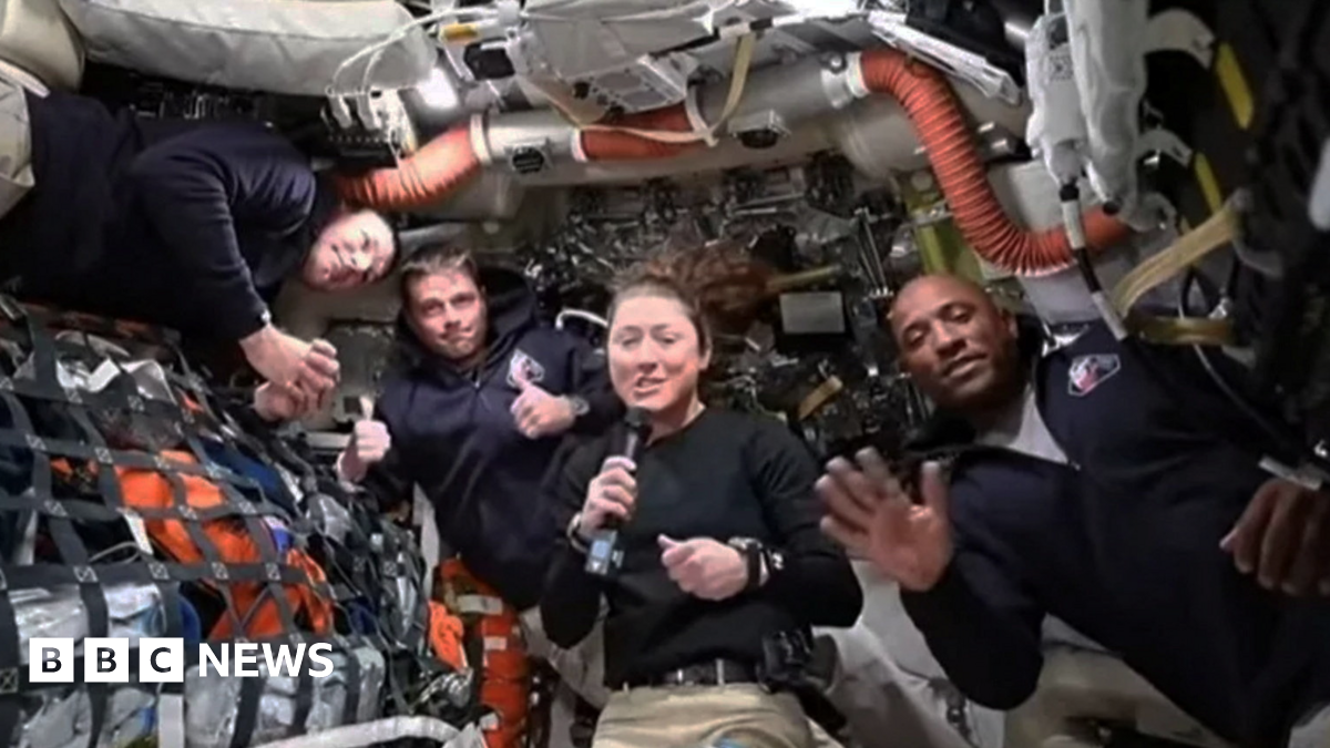A section of the Orion spacecraft on the bottom left corner with the moon in the background filling the right side with half of it in darkness.
