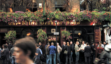 London pub exterior with historic architecture and patrons enjoying drinks on a sunny day, highlighting local social culture.