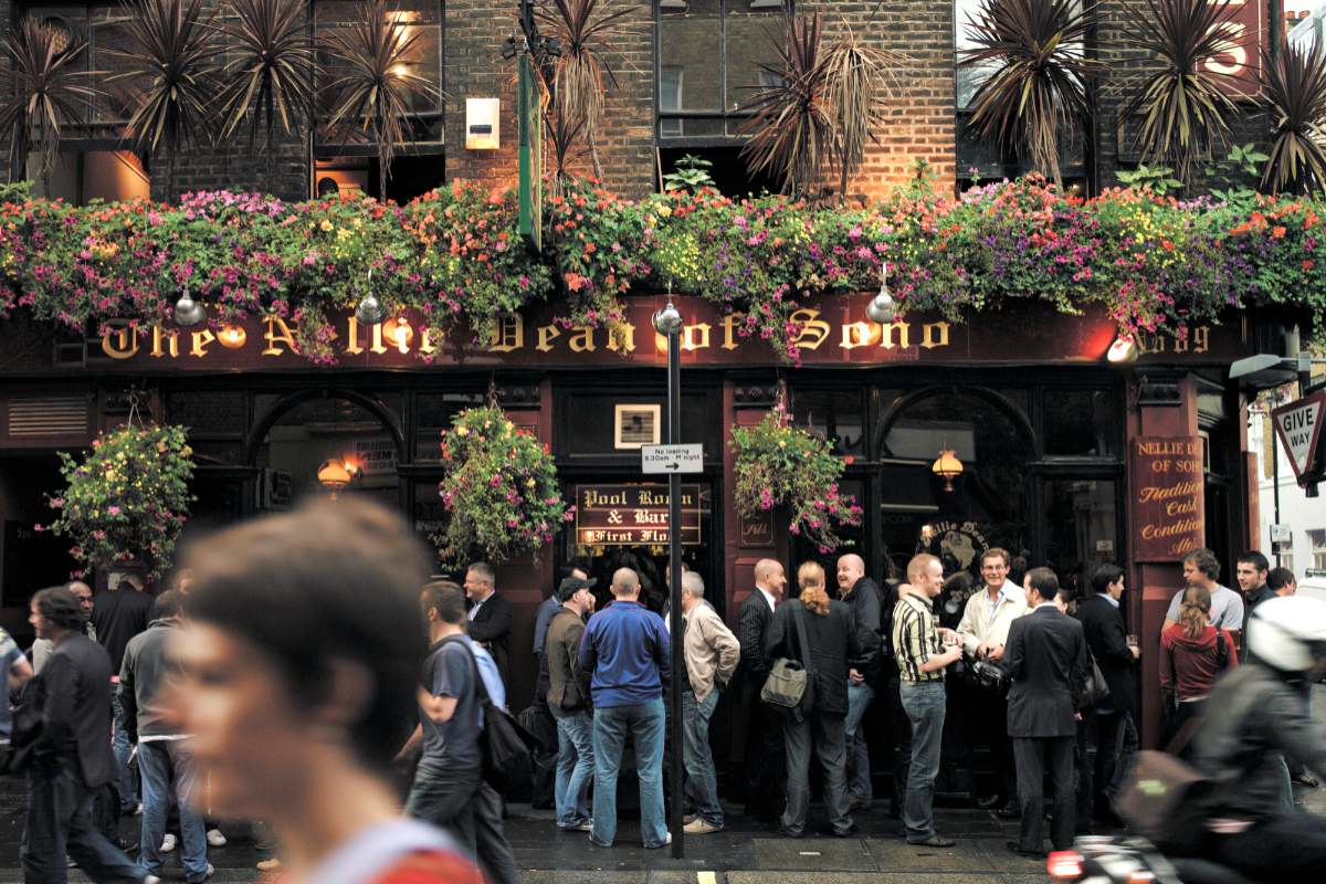 London pub exterior with historic architecture and patrons enjoying drinks on a sunny day, highlighting local social culture.