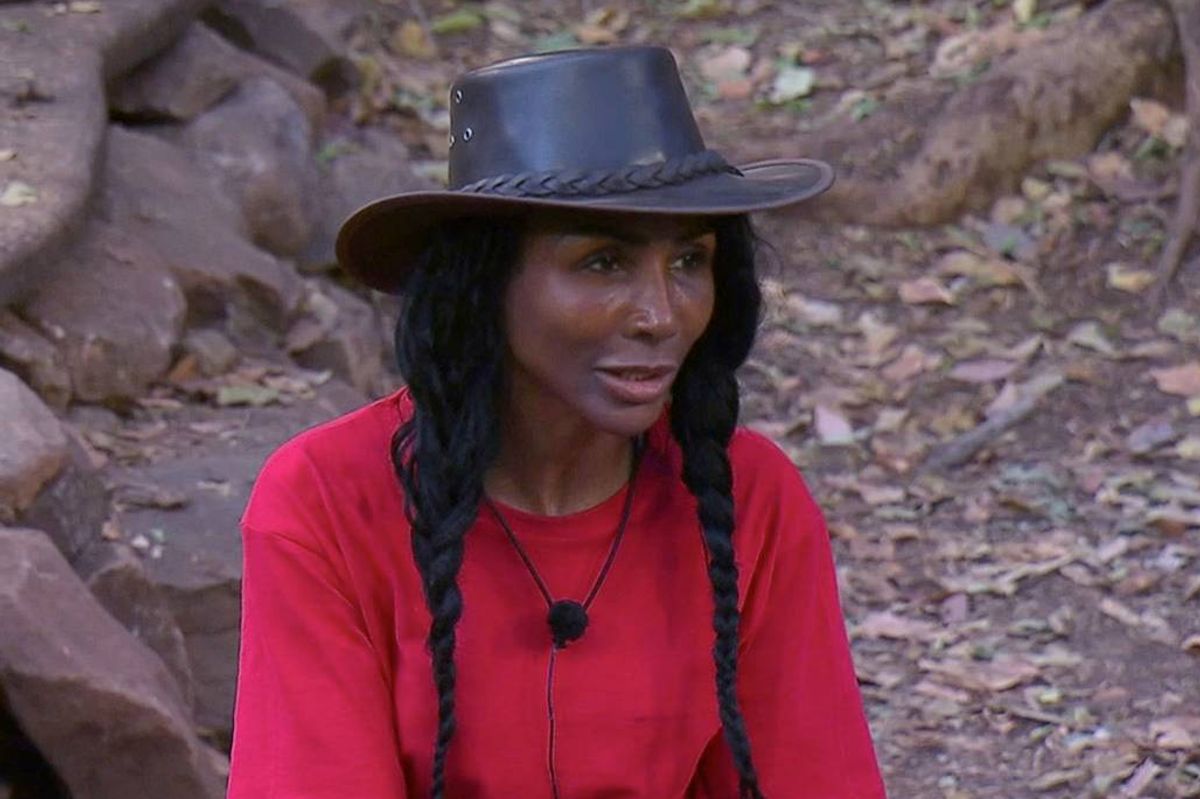 sinitta in red with black hat in jungle 2026