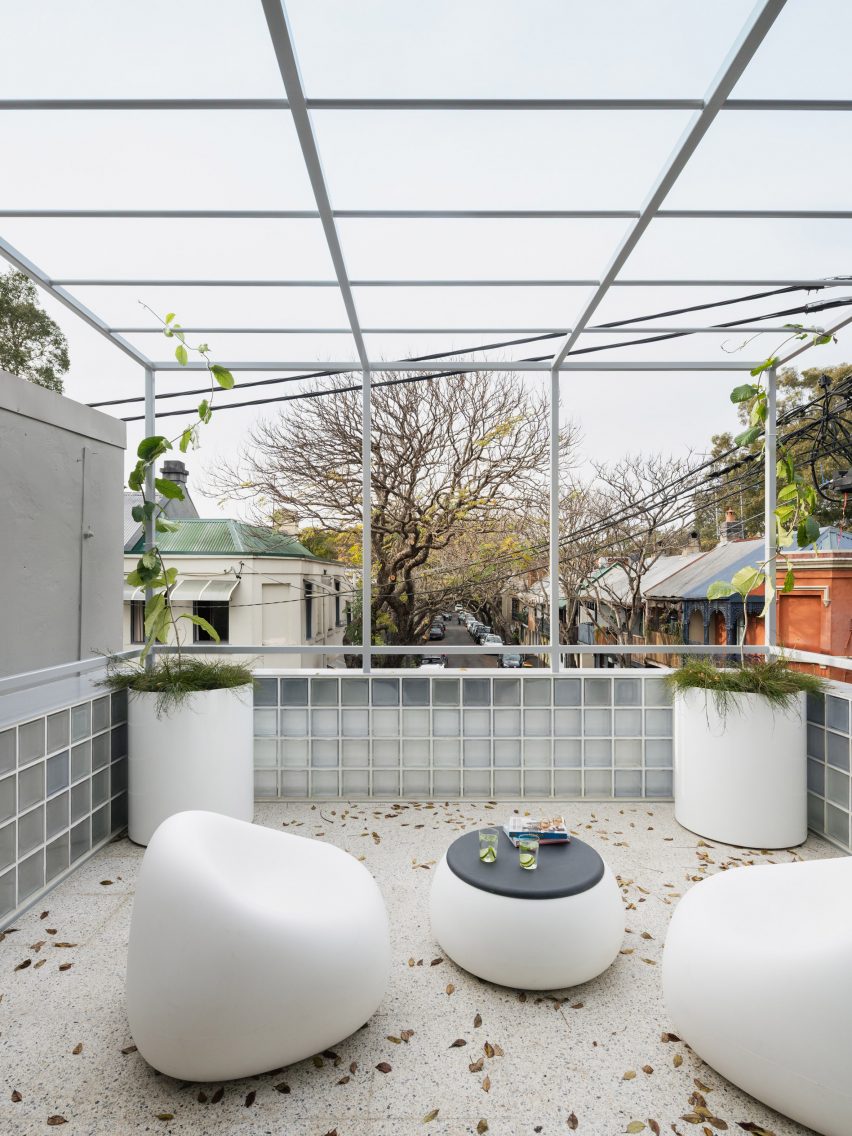 A terrazzo floored terrace with white furniture and a steel overhead structure in The Corner House
