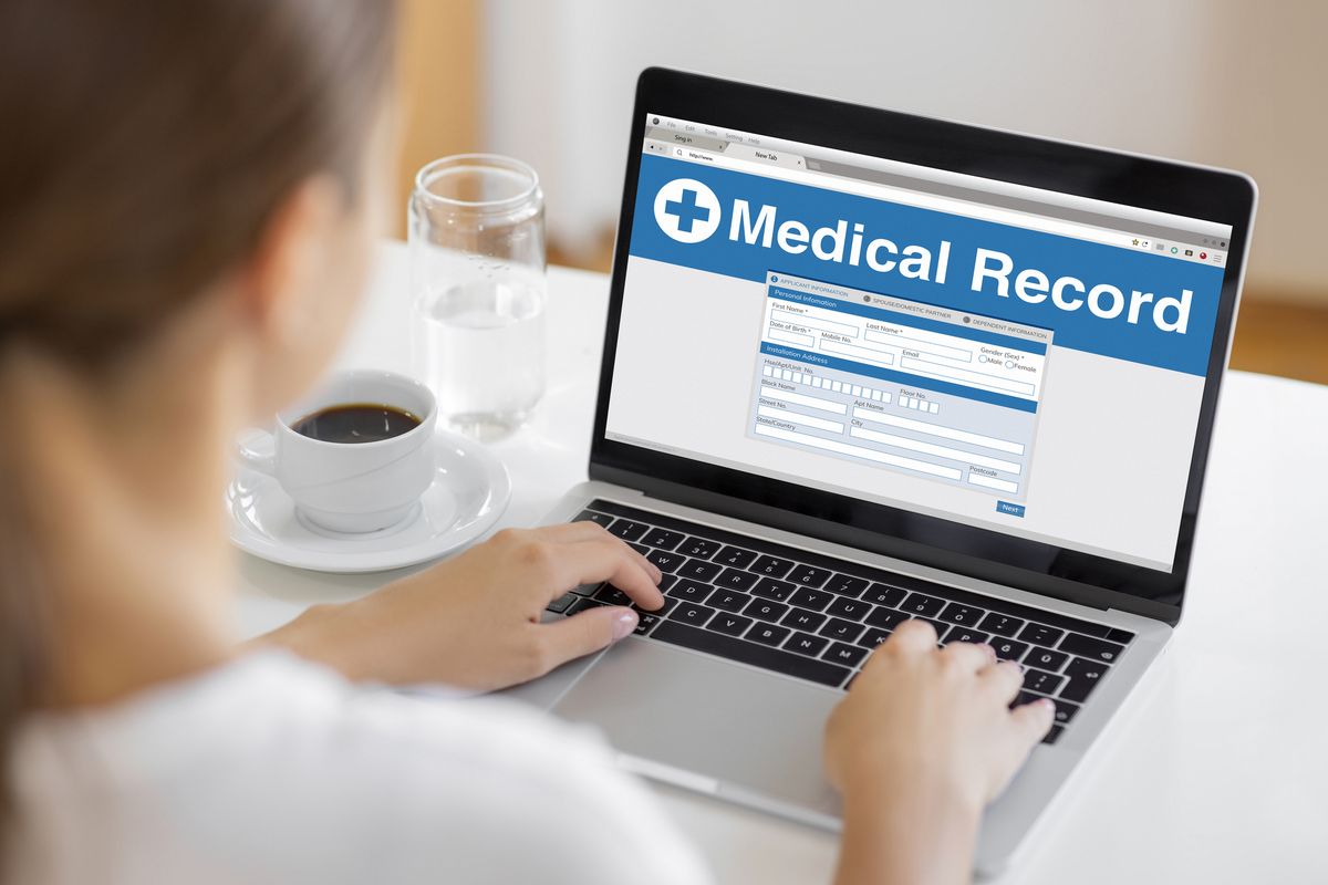 A woman reviews her medical records on a laptop, with a coffee cup and water nearby, symbolizing digital healthcare management, personal health tracking, and patient data access.