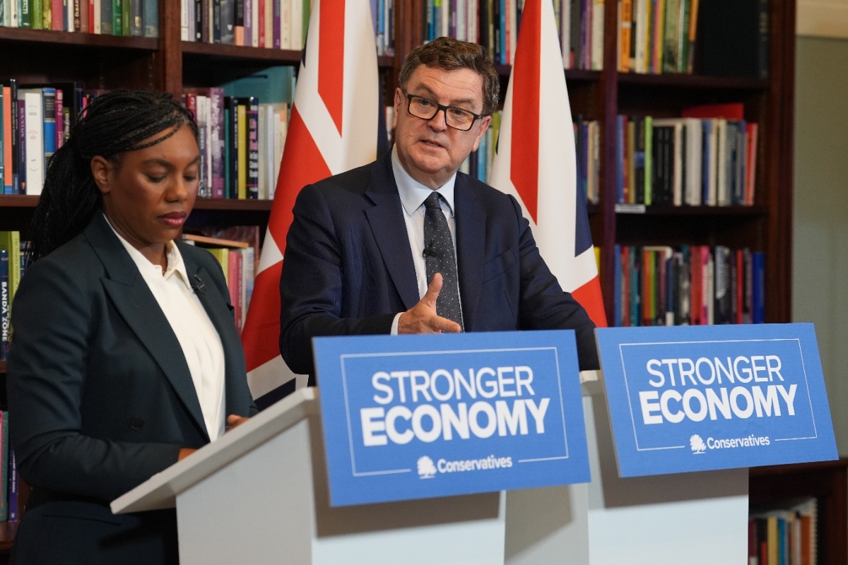 Mel Stride speaking at a press conference, addressing key issues, in a formal setting with a backdrop of the events logo.