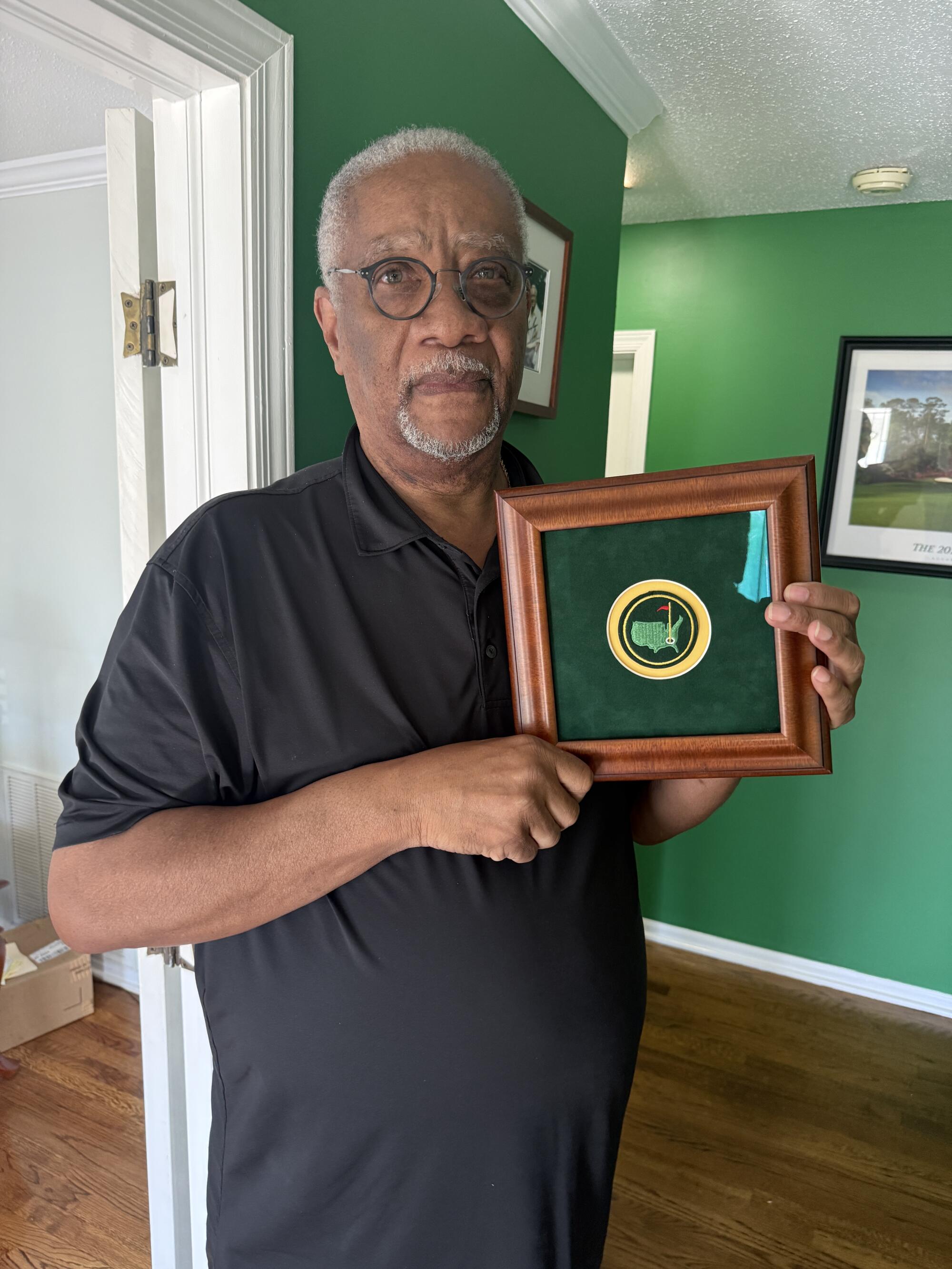 Lawrence Bennett, a longtime chauffeur at Augusta National, holds a framed portion of the logo.