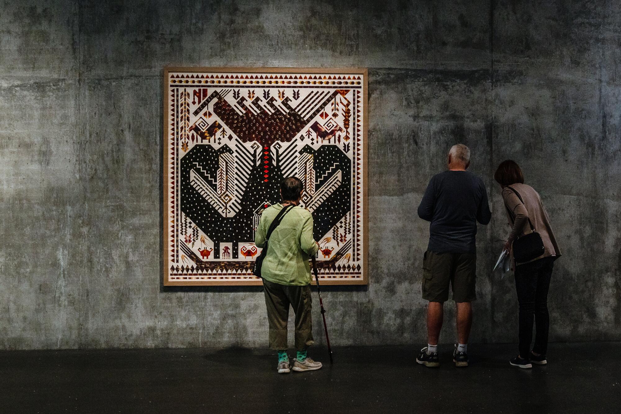 Three people stand in front of "Tampan World Mountain, Ancestral Creatures, 2022" on view in a museum.
