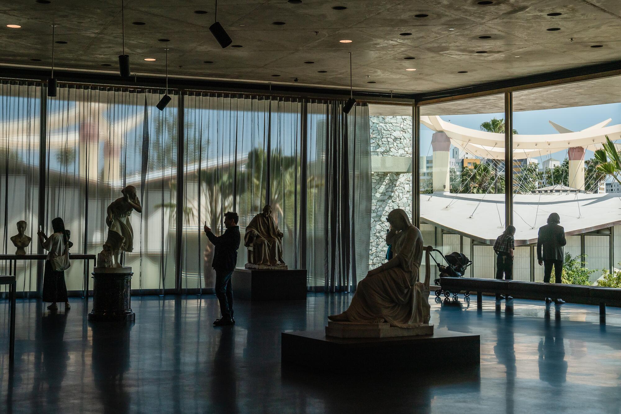 Sculptures inside a museum with floor-to-ceiling windows.