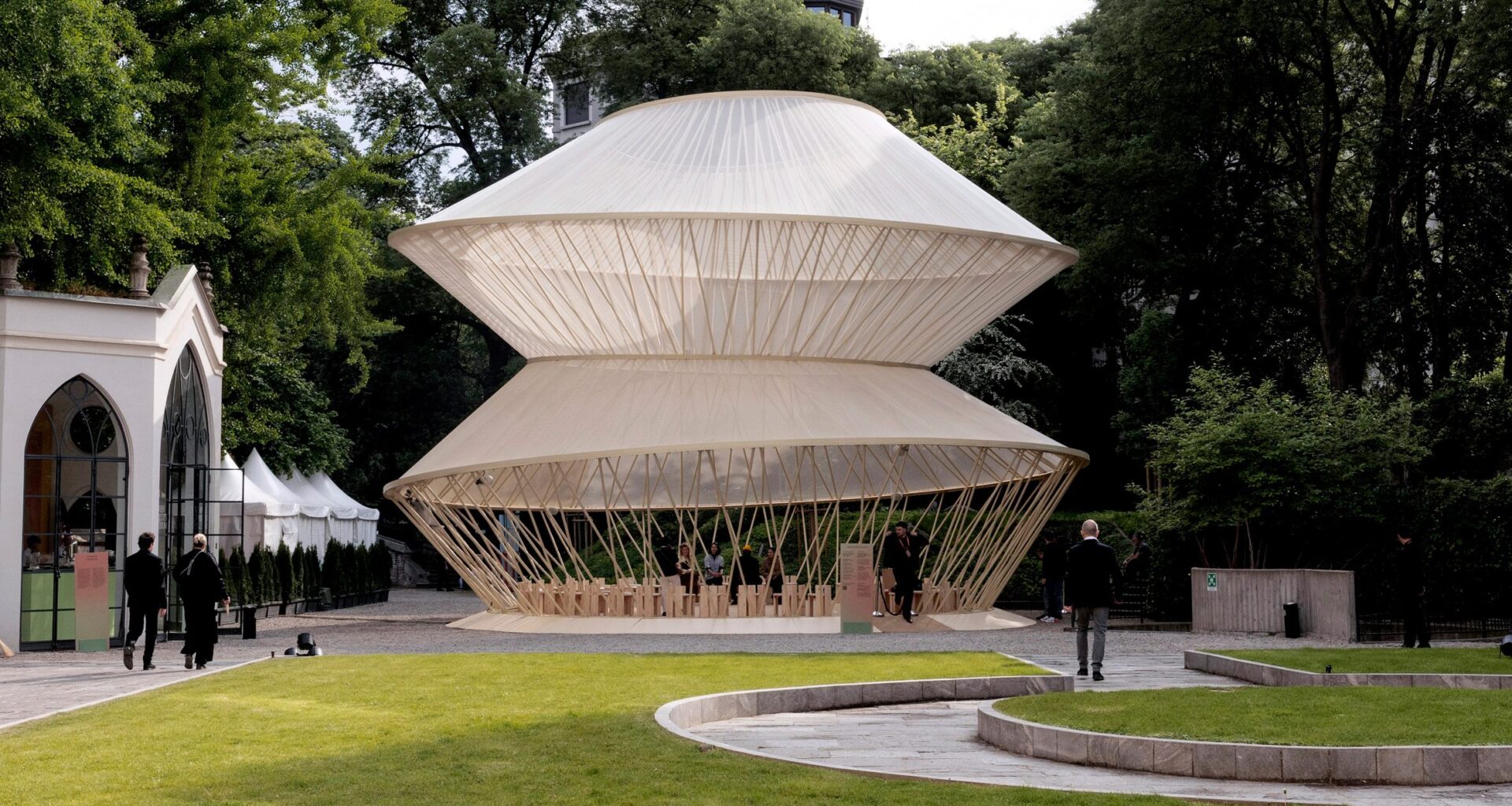 Garden setting with the yurt pavilion surrounded by trees and visitors walking nearby