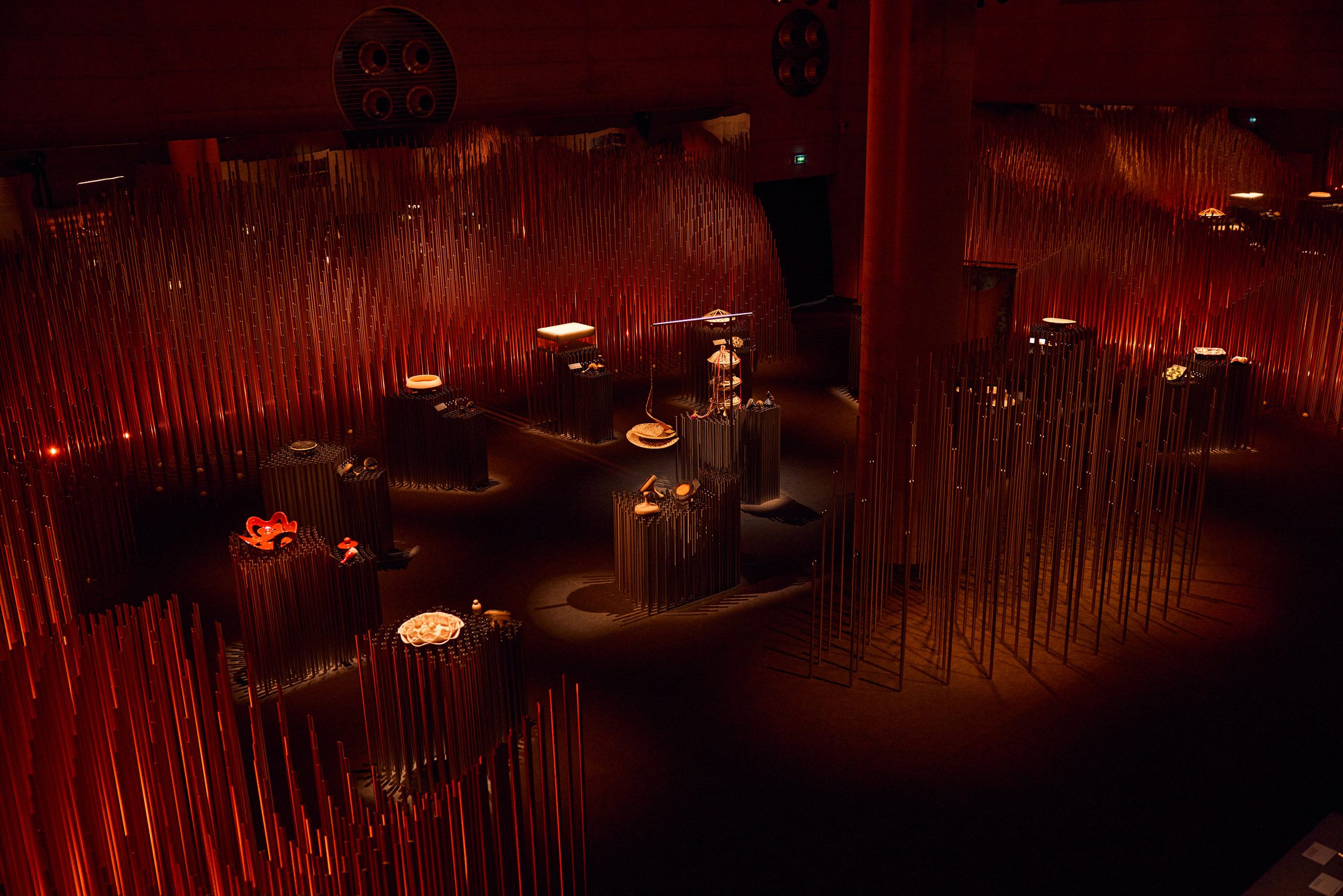 Exhibition with red lighting and dense vertical rods surrounding display plinths