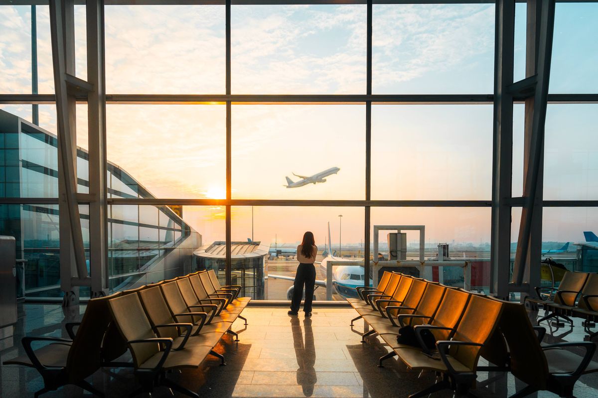 A young Asian woman is using a smartphone to check the arrival departure board and flight schedule at the airport.