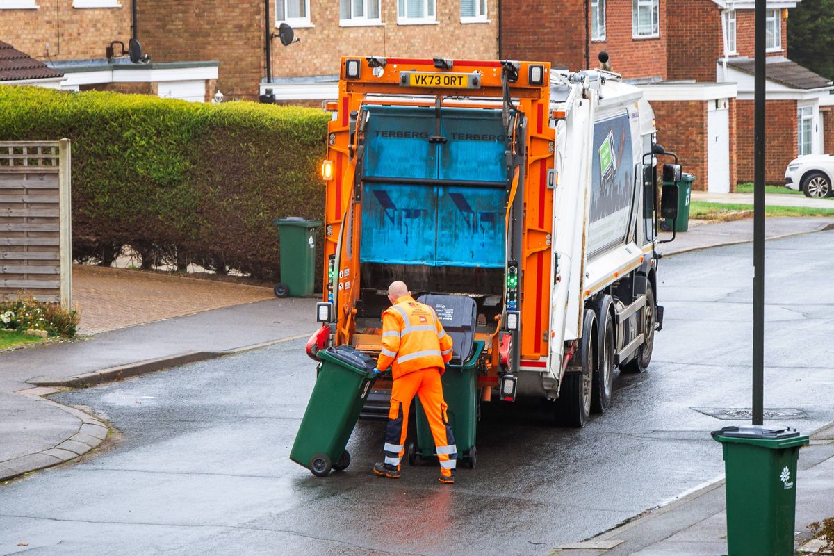 Elevated view of a garbage truck and a waste collection worker loading trash bins into the truck on a residential street in southeast England.