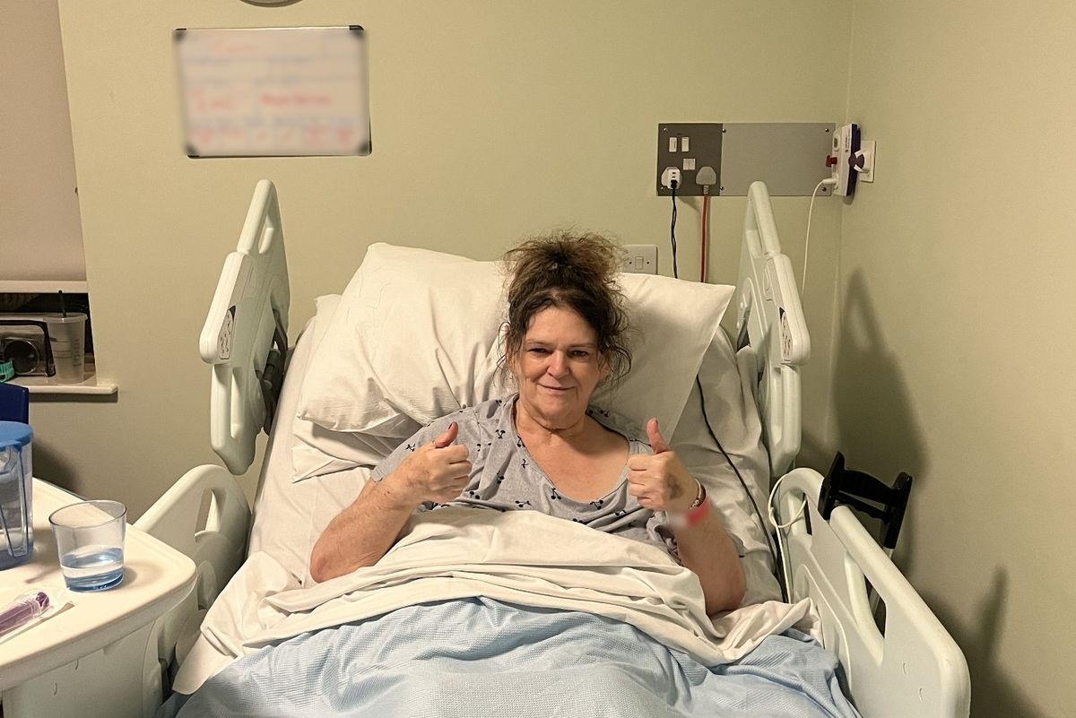 Carol giving thumbs up signs from a hospital bed