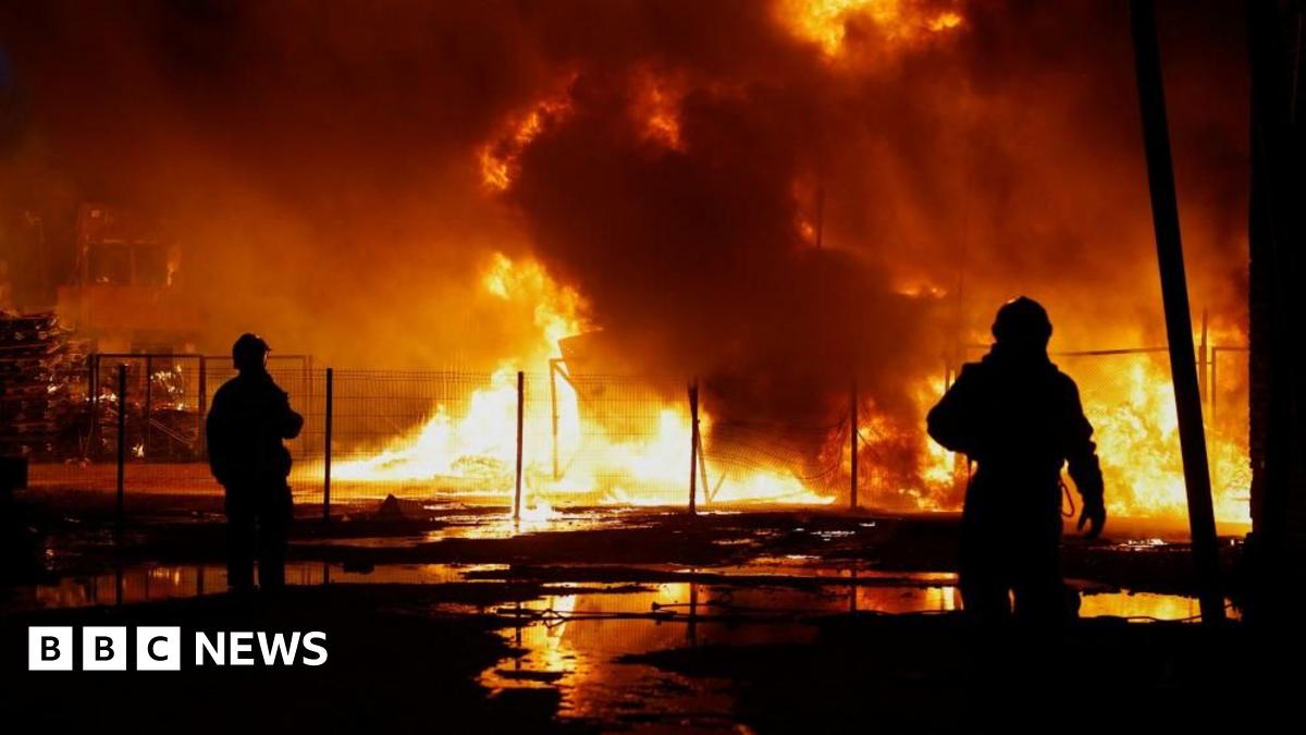 Two rescuers are silhouetted against a backdrop of fire in Kyiv