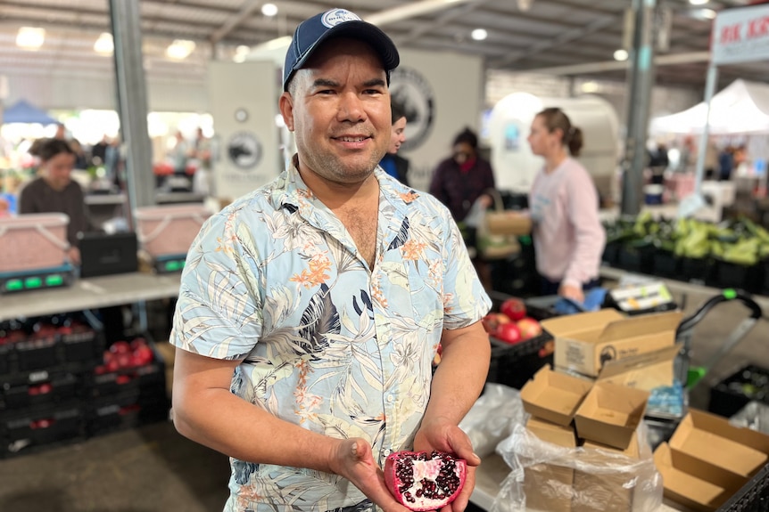 A man smiles near a stall in a market.