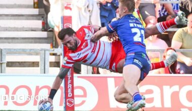 St Helens wing Kyle Feldt, in red and white, reaches out to score a try by the corner flag as Jayden Myers, in blue, tries to push him into touch.