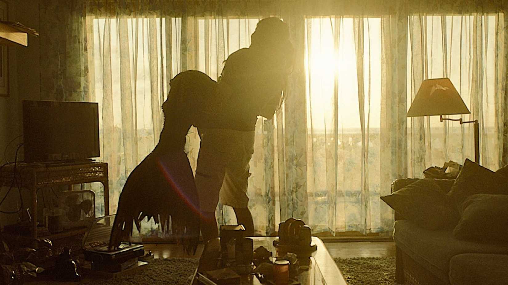 An image from Mermaid 2025. It shows a man hoisting a mermaid into his arms while the sun shines in from the window.