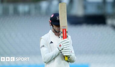 Ollie Price of Gloucestershire walks off the pitch with his bat held up towards the sky covering his face