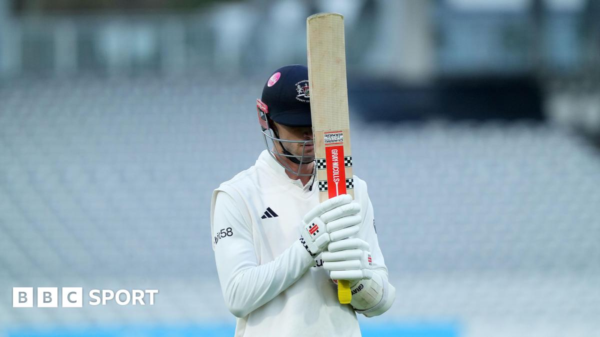 Ollie Price of Gloucestershire walks off the pitch with his bat held up towards the sky covering his face