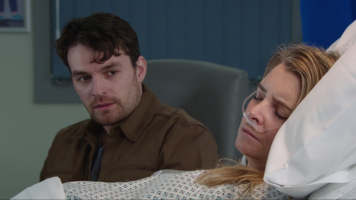 22_04_emm_charity Mack watches Charity, who is lay in a hospital bed asleep, in a scene from Emmerdale