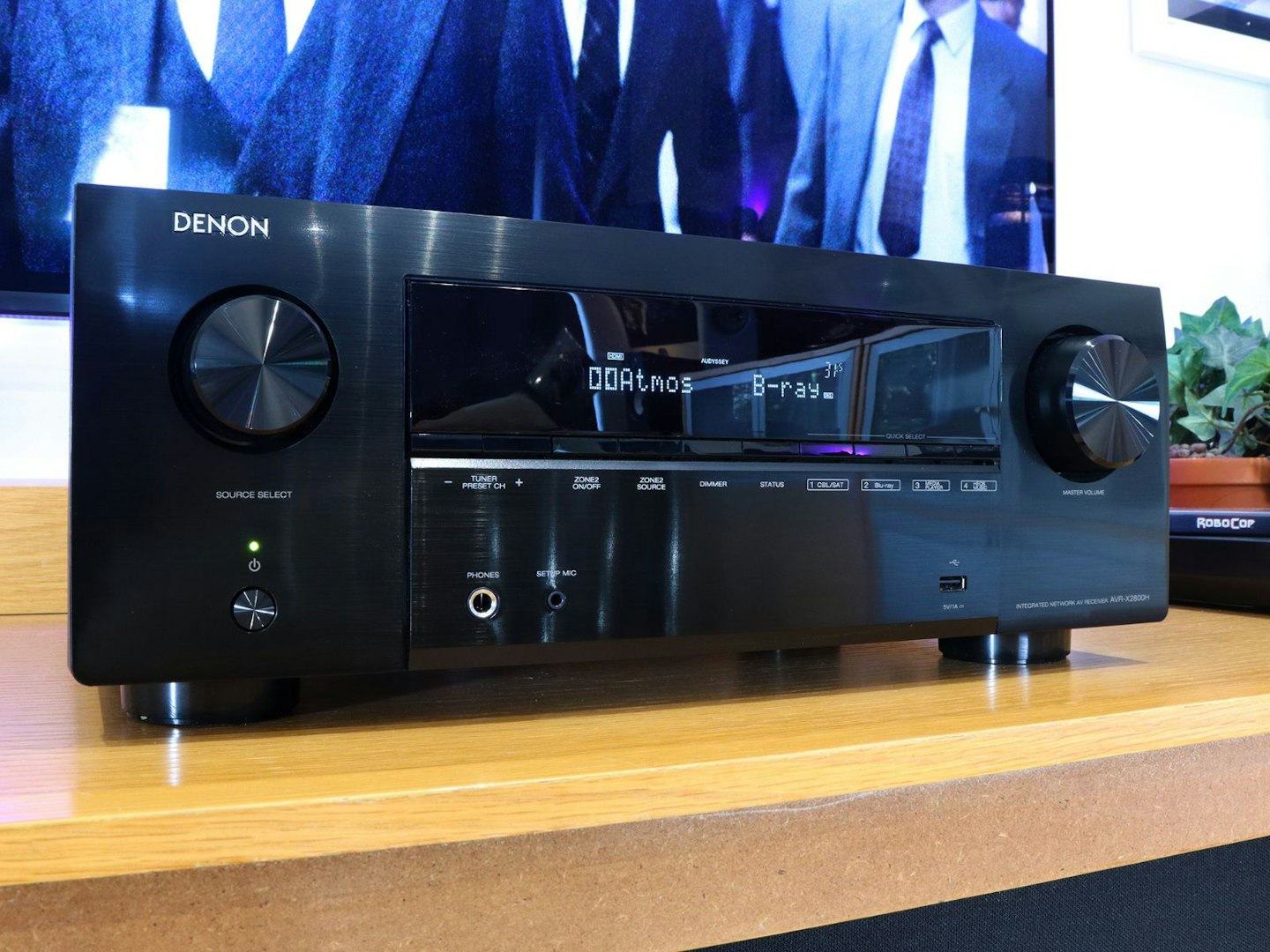 Denon AVR-X2800H Home Cinema Amplifier with dolby atmos display on a stand in front of a TV