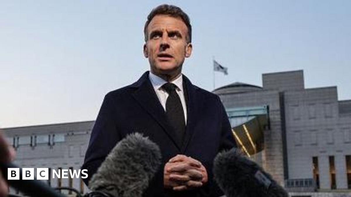 A woman and a man in black jackets look out over Tehran's skyline with a tall tower in the distance. They have their backs to the camera, she has long brown hair tied in a pony tail and her right hand rests on his left shoulder.