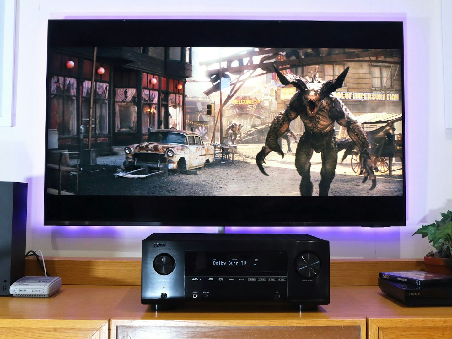 Denon AVR-X2800H Home Cinema Amplifier on a stand in a living room with xbox and snes console in front of a TV showing Fallout