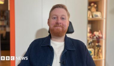 Michael Campbell has a ginger beard and blue eyes. The top of his wheelchair is visible behind his head. He is wearing a navy shirt with a white T-shirt underneath.
