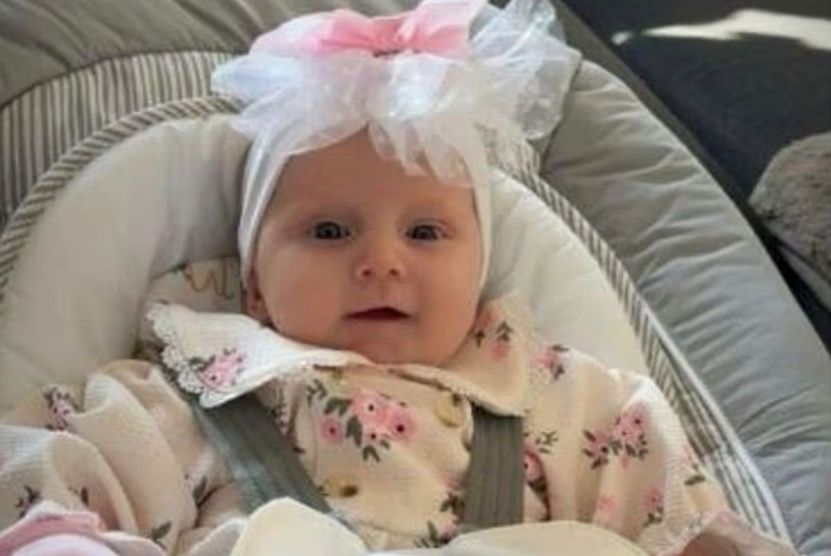 A picture of Maggie-May Ann Moody in a baby chair wearing a flowery top and headdress