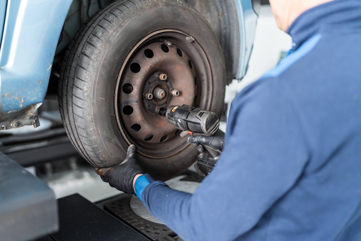 Mechanic working on a vehicle tire using an electric screwdriver in a car repair shop