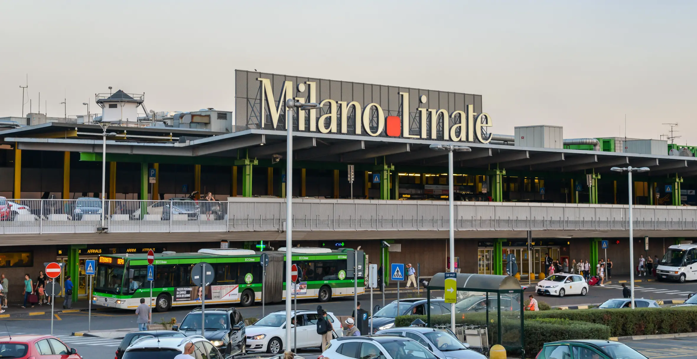 Milan Linate airport in Italy, with a large sign displaying "Milano Linate" on the building, buses, and cars parked outside.